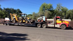 Low-bed hauling backhoe, mini excavator and bobcat to job site