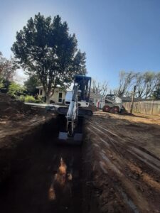 Mini excavator digging trench in back yard with mini bobcat