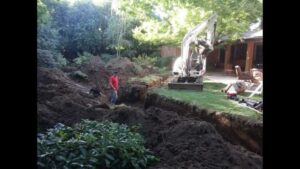 Backyard of house with trees and grass, site work with mini excavator digging trench