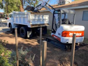 Site work in chico, ca side of house with mini excavator loading a dump truck